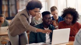 Three students gathered around a laptop looking at it together