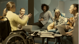 Small group of students in a lounge talking. One person is using a wheeled chair.