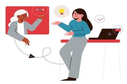 Two females have a discussion. One woman in a turquoise shirt and gray pants is leaning on a desk while the second a white haired woman with a grey sweater is on a screen.