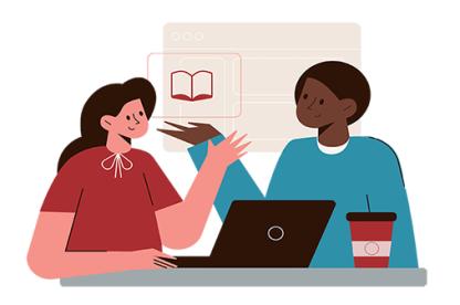 Two instructors, one white woman in a red shirt with bow and one black male instructor with a turquoise shirt sit at a desk and engage in a discussion. 